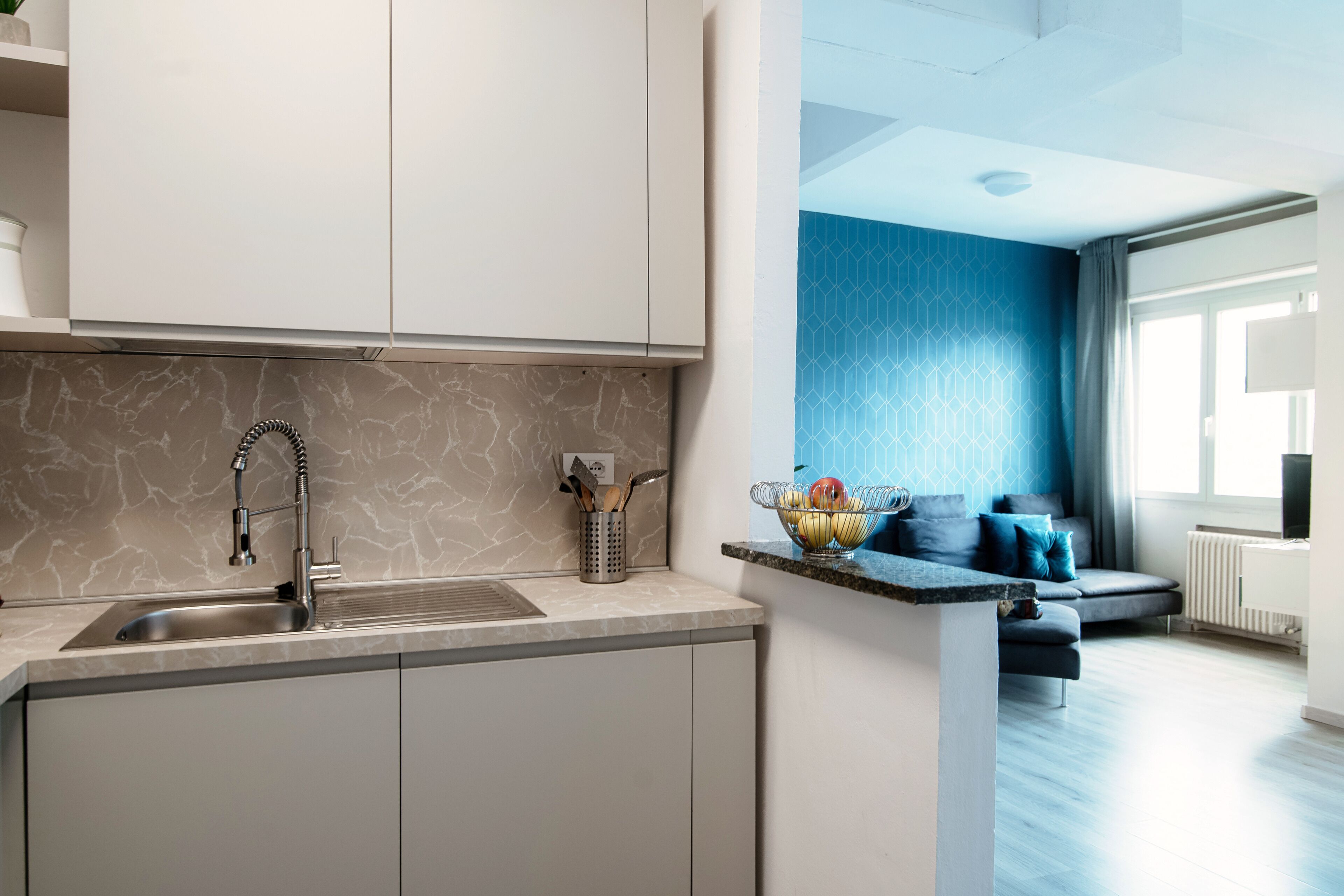 A modern kitchen with a marble backsplash, a stainless steel sink, and a countertop with a fruit bowl.