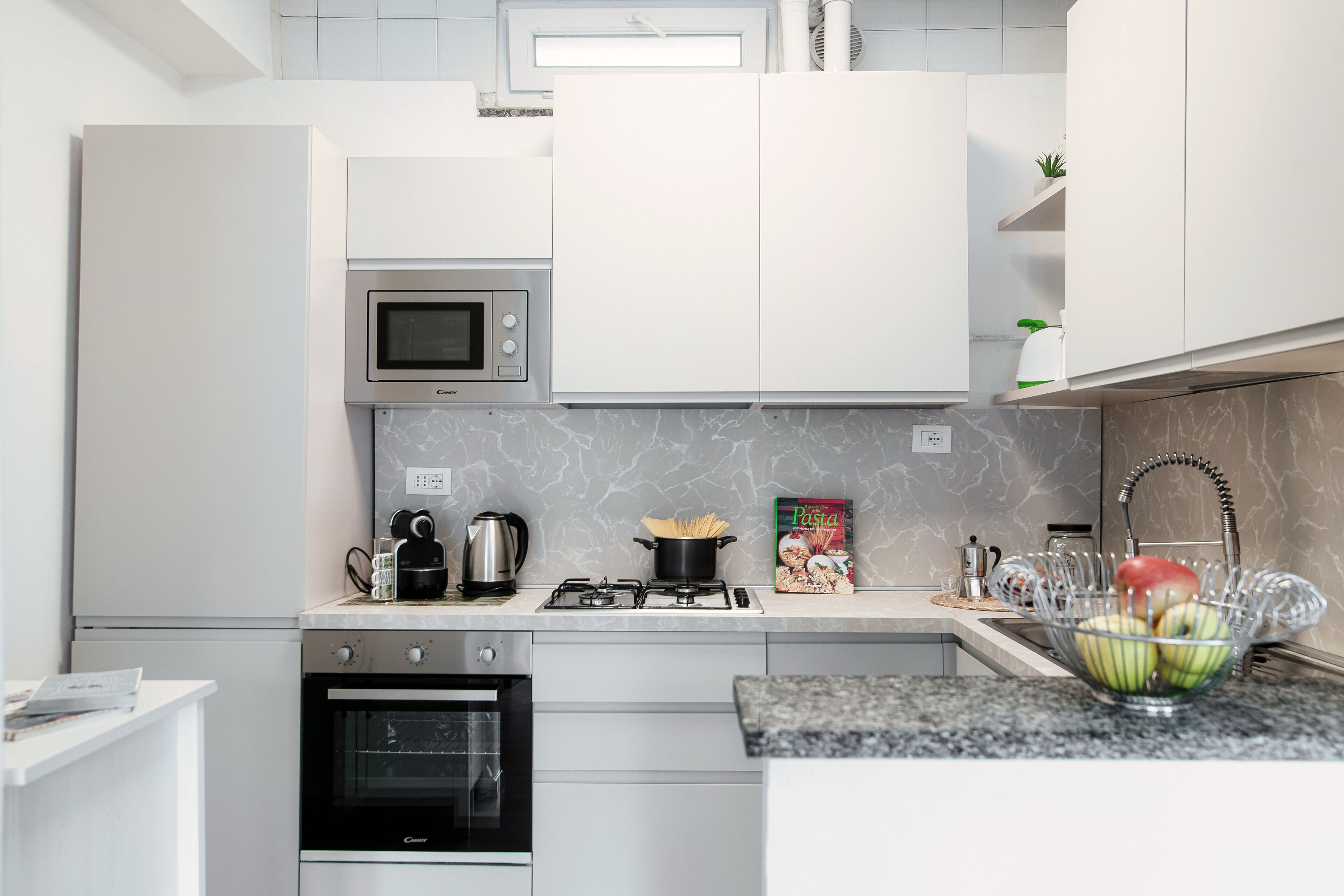 A modern kitchen with white cabinets, a built-in microwave, a gas stove, and a sink with a fruit bowl.