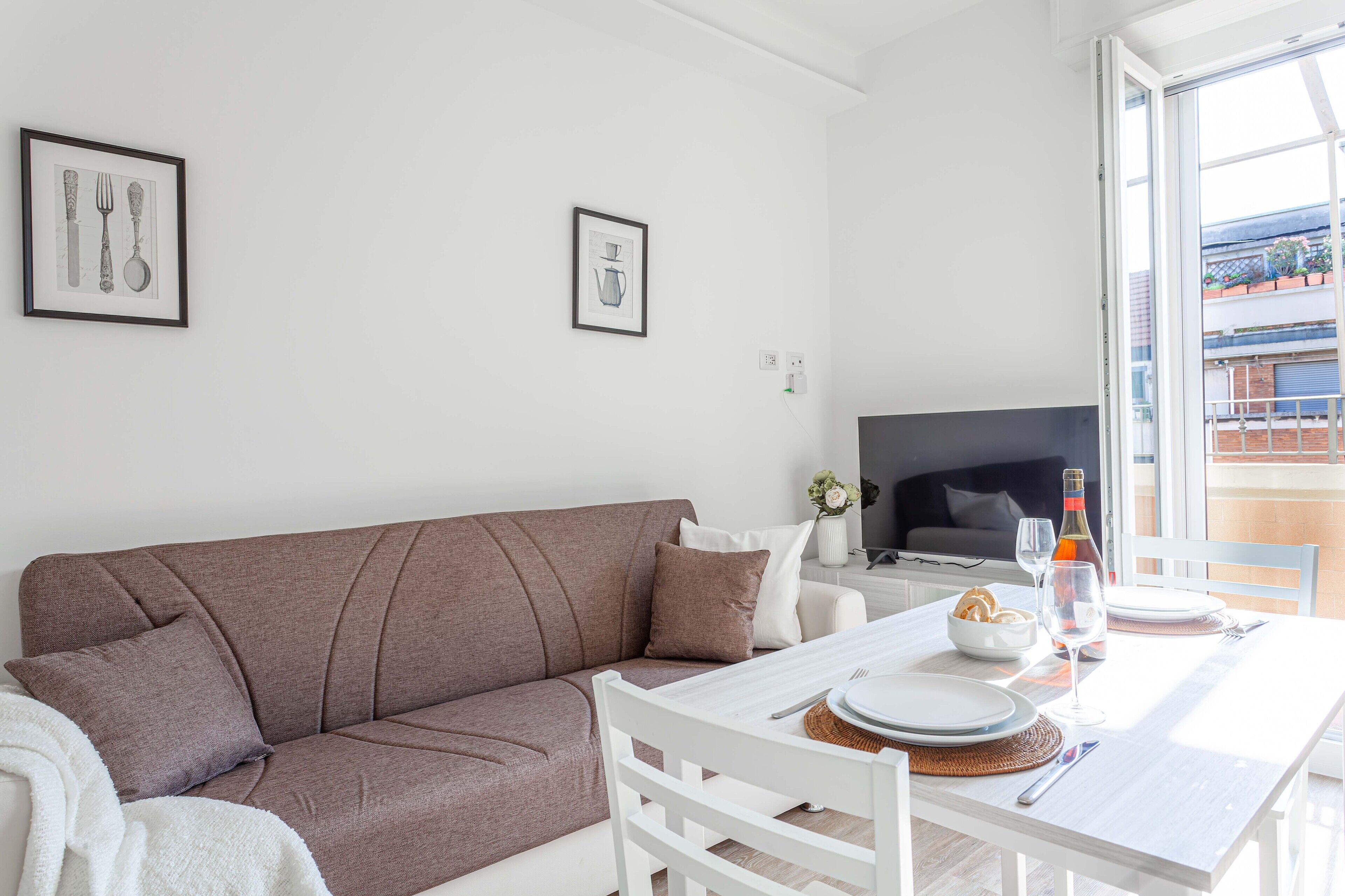 Ein modernes Wohnzimmer mit einem braunen Sofa, einem weißen Esstisch und einem Fernseher.