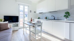 A modern kitchen with white cabinets, a dining area with a white table and chairs, and a television on a white sofa.