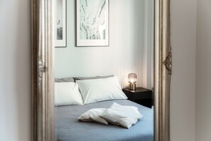 Une chambre à coucher avec un lit, des oreillers, une table de chevet, une lampe et des œuvres d’art encadrées accrochées au mur.