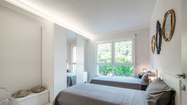 Ein modernes Schlafzimmer mit zwei Betten, einem großen Fenster und einem Spiegel an der Wand.