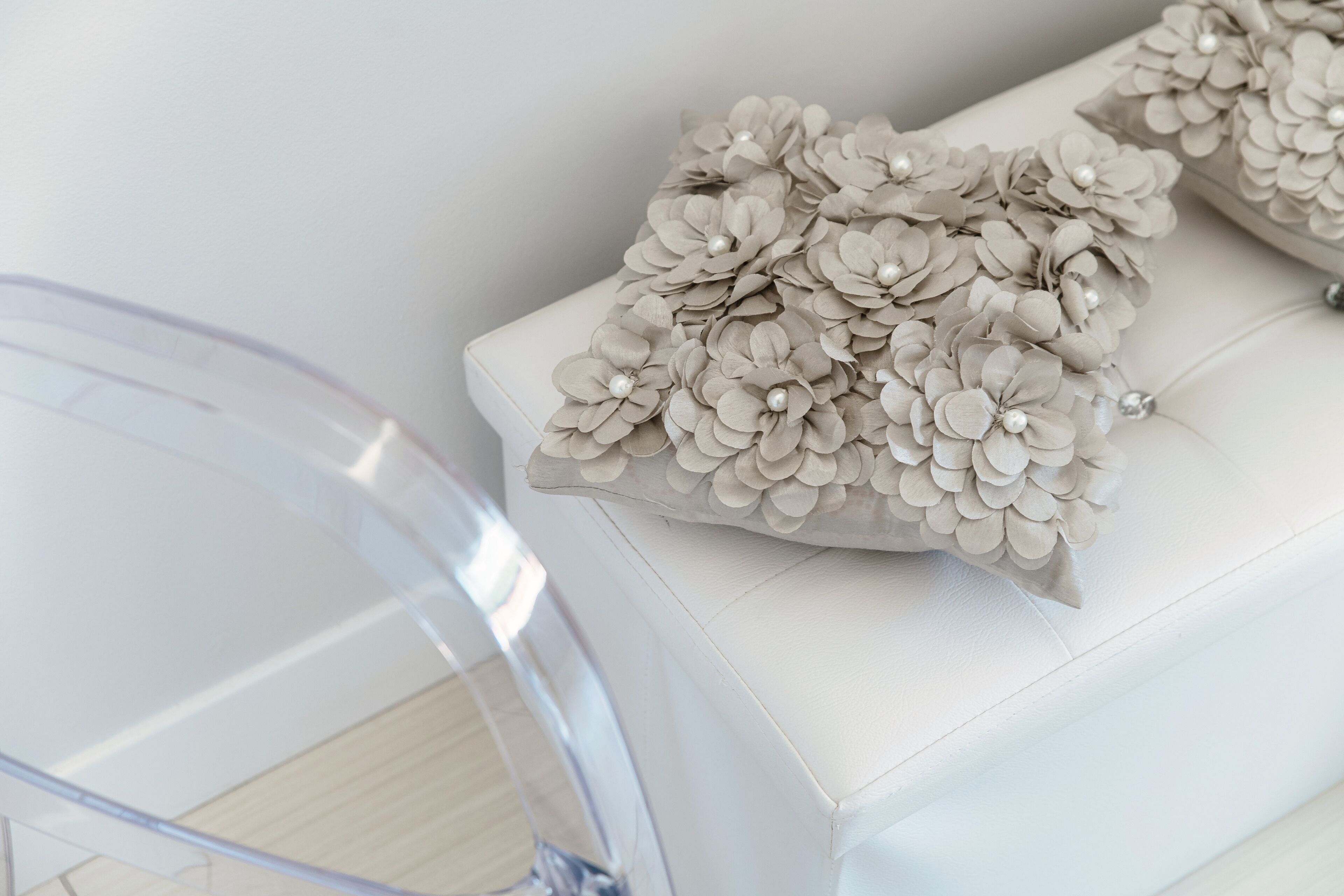 A white sofa with a floral cushion and a clear glass coffee table.