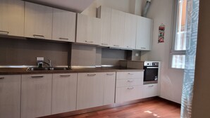 A modern kitchen with light wood cabinets, stainless steel appliances, and a window with a view. - JOIVY Studio Near Porta Romana (Milan)