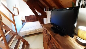 A bedroom with a bed, wooden dresser, television, and a lamp.