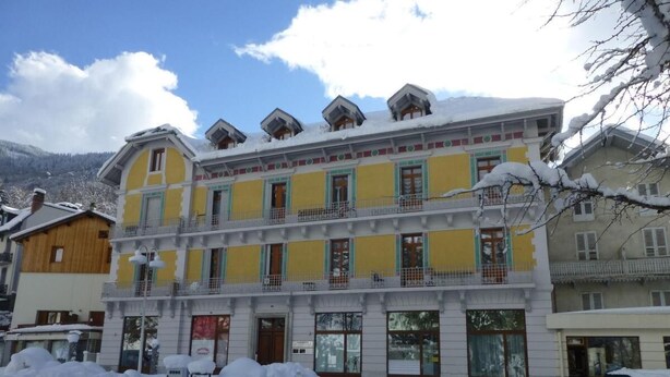 A multi-story building with balconies, a snow-covered ground, and a mountainous backdrop.