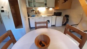 A compact kitchen with white cabinets, a wooden dining table, and a chair.