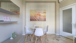 A dining area with a round table and four white chairs, a painting of a sunset over a cityscape, and a door with a frosted glass panel. - JOIVY Trendy Flat W/Balcony (Milan)