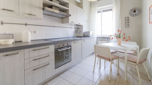A modern kitchen with white cabinetry, a built-in oven, and a dining area with a white table and chairs. - JOIVY Trendy Flat W/Balcony (Milan)