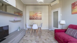 A modern living room with a flat-screen TV, a red sofa, a dining area with a table and chairs, and a large abstract painting on the wall. - JOIVY Trendy Flat W/Balcony (Milan)