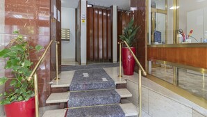 A hotel lobby with marble flooring, a reception desk, and a staircase with red potted plants. - JOIVY Trendy Flat W/Balcony (Milan)