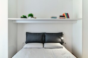 A bedroom with a bed, two pillows, a shelf with books and plants, and a wall-mounted light. - JOIVY Superb Flat W/Balcony (Como)