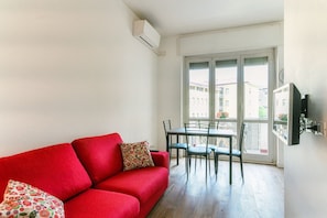 A red sofa with floral cushions, a dining table with chairs, and a balcony with a view of buildings. - JOIVY Superb Flat W/Balcony (Como)
