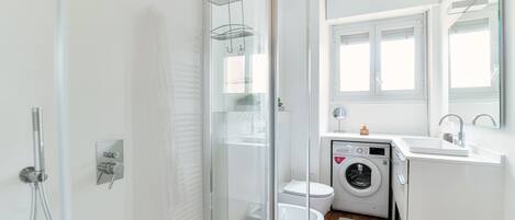 Une salle de bain moderne avec une douche à parois de verre, des toilettes, un lave-linge et un lavabo avec un miroir.