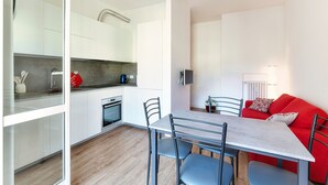Una cocina moderna con armarios blancos, una mesa de comedor con sillas y un sofá rojo en un salón luminoso.