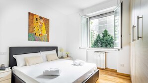 Une chambre à coucher moderne avec un grand lit, une fenêtre donnant sur la verdure et un tableau accroché au mur.