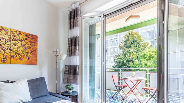 Une chambre moderne avec un canapé, une petite table agrémentée d’une plante, et un balcon équipé d’une table et de chaises.