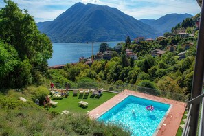 A swimming pool with a mountain view, surrounded by lush greenery and residential buildings. - JOIVY Luxury flat & Lake Como view (Argegno)