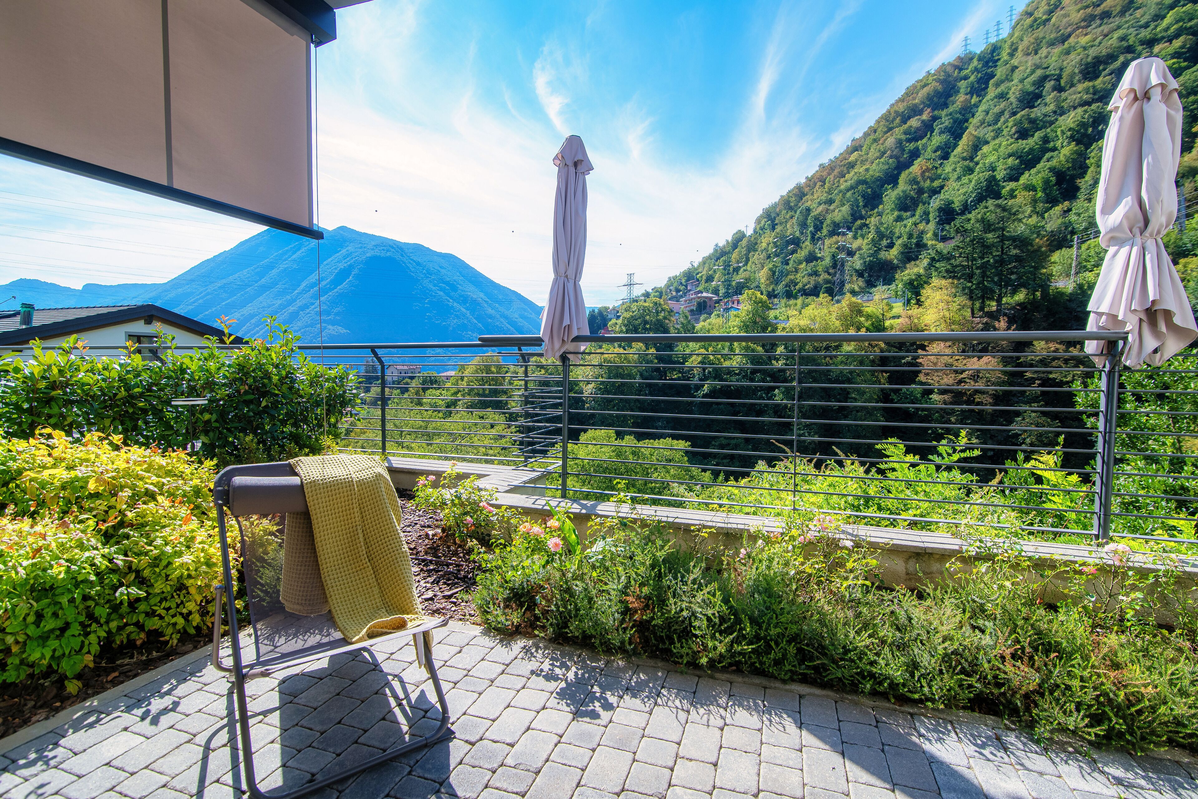 A balcony with a metal railing, a bench with a yellow towel, and a view of a mountain and greenery.