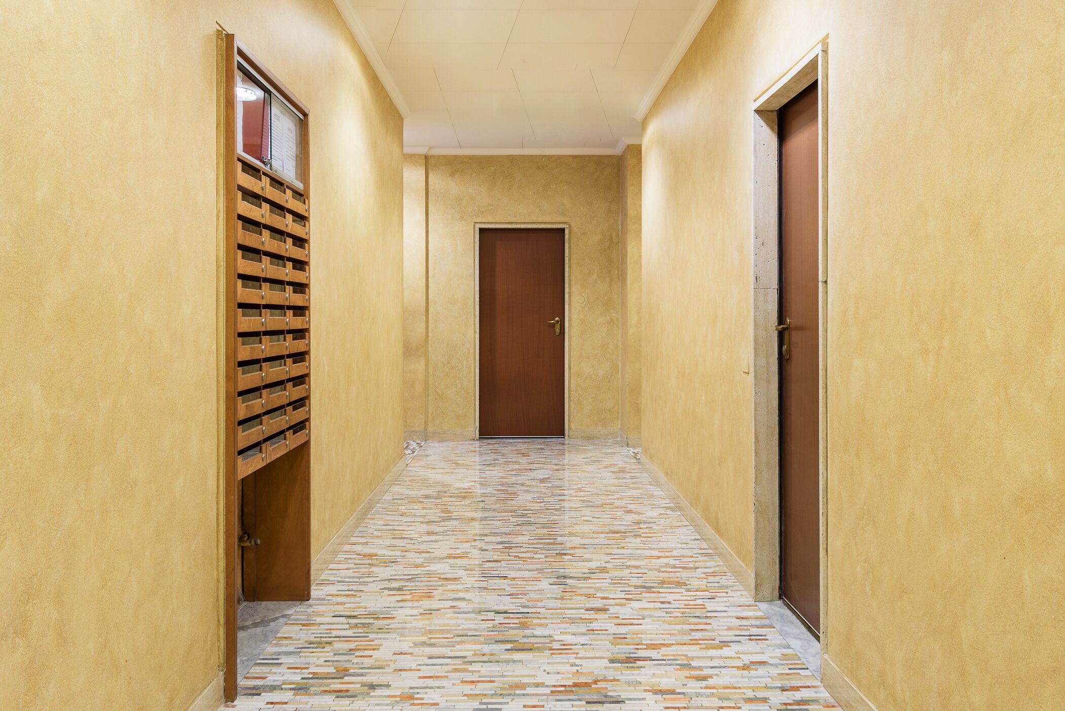 Un couloir avec un sol à motifs, des casiers en bois et une porte au fond.