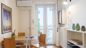 A room with a wooden dining table, two chairs, a radiator, a TV mounted on the wall, and a bookshelf with books and decorative items. - JOIVY Homey 1-Bed W/View Near Citylife (Milan)