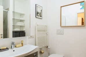 Une salle de bain avec un lavabo blanc, un miroir, un porte-serviettes et des toilettes.