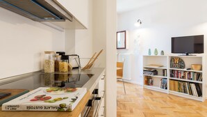 A modern kitchen with a built-in stove, a microwave, and a range hood. There is a bookshelf filled with books and decorative items. - JOIVY Homey 1-Bed W/View Near Citylife (Milan)