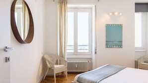 A bedroom with a bed, a chair, a large mirror, a radiator, and a window with curtains. - JOIVY Homey 1-Bed W/View Near Citylife (Milan)