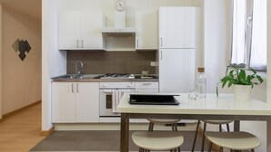 A modern kitchen with white cabinets, a stove, and a dining table with chairs. - JOIVY 1-Bed Flat In Quiet Neighborhood (Milan)