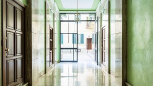 A hallway with a polished floor, a chandelier, and a view of a building with a balcony. - JOIVY 1-Bed Flat In Quiet Neighborhood (Milan)