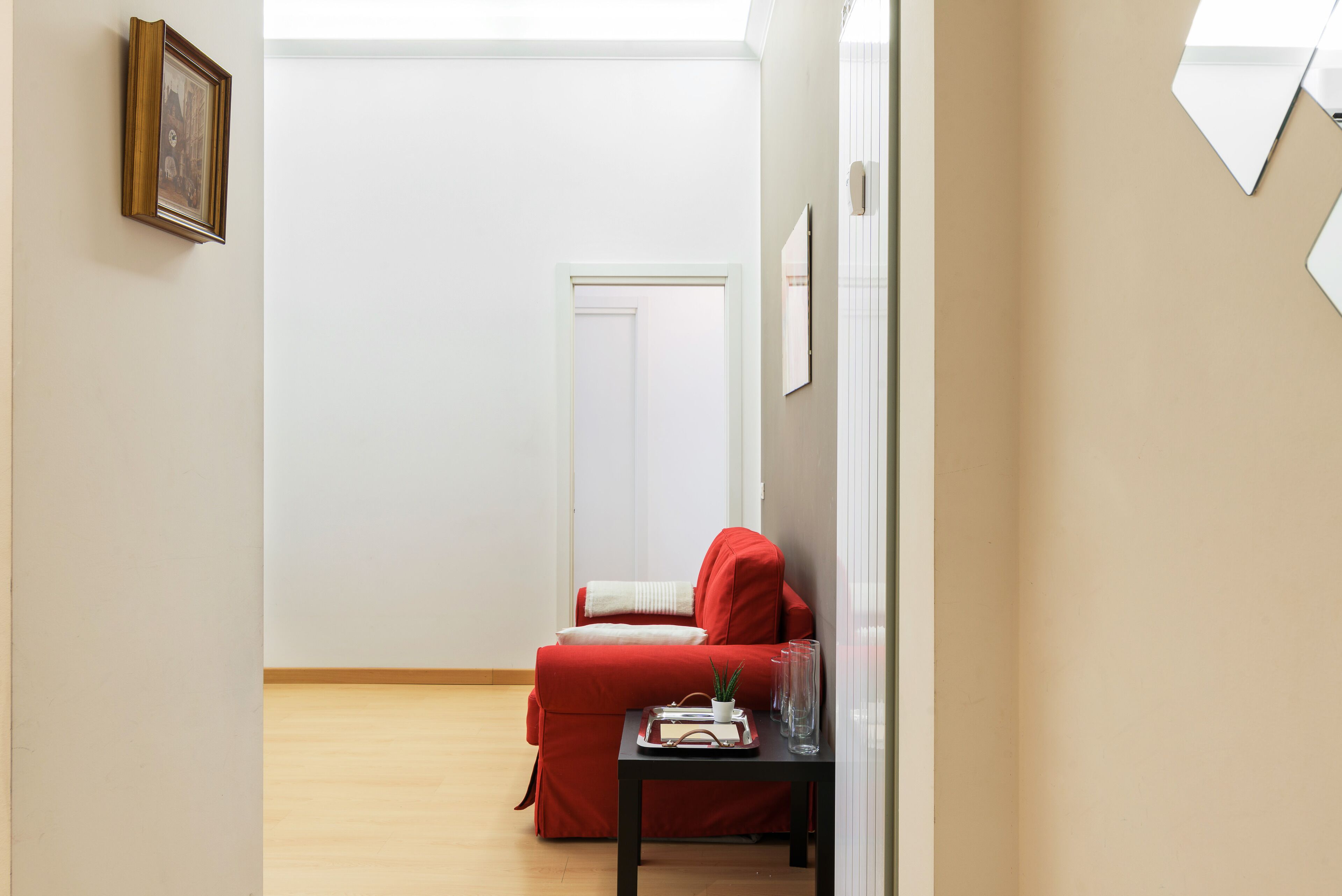 A minimalist living room with a red sofa, a small table with a tray, and a framed picture on the wall.