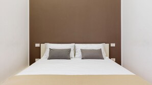 A bed with white bedding and two gray pillows, set against a brown wall with a white headboard. - JOIVY 1-Bed Flat In Quiet Neighborhood (Milan)