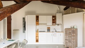 A modern kitchen with white cabinets, a wooden cabinet, and a dining area with a table and chairs. - JOIVY Classic Top-Floor Studio By Park (Milan)