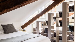 A bedroom with a sloped ceiling, a bed with a grey blanket, and a white headboard. There are white shelving units with black storage boxes. - JOIVY Classic Top-Floor Studio By Park (Milan)