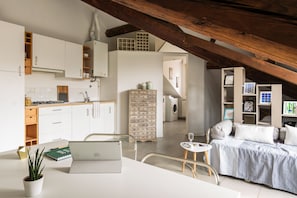 Een moderne keuken met witte kasten, een eethoek met een laptop, en een gezellige zithoek met een bed.