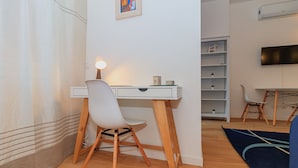 A compact room with a white desk, a chair, a lamp, a bookshelf, and a TV mounted on the wall. - JOIVY Cosy 1Bed Flat In Fiera (Milan)