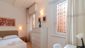 A bedroom with a bed, a desk, a chair, a dresser, and a window with a view of buildings. - JOIVY Cosy 1Bed Flat In Fiera (Milan)