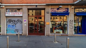 A storefront with a closed shutter, a sign for B&G TAPPETI, and a blue awning for a shop named "Passione abbellimento uomo". - JOIVY Cosy 1Bed Flat In Fiera (Milan)