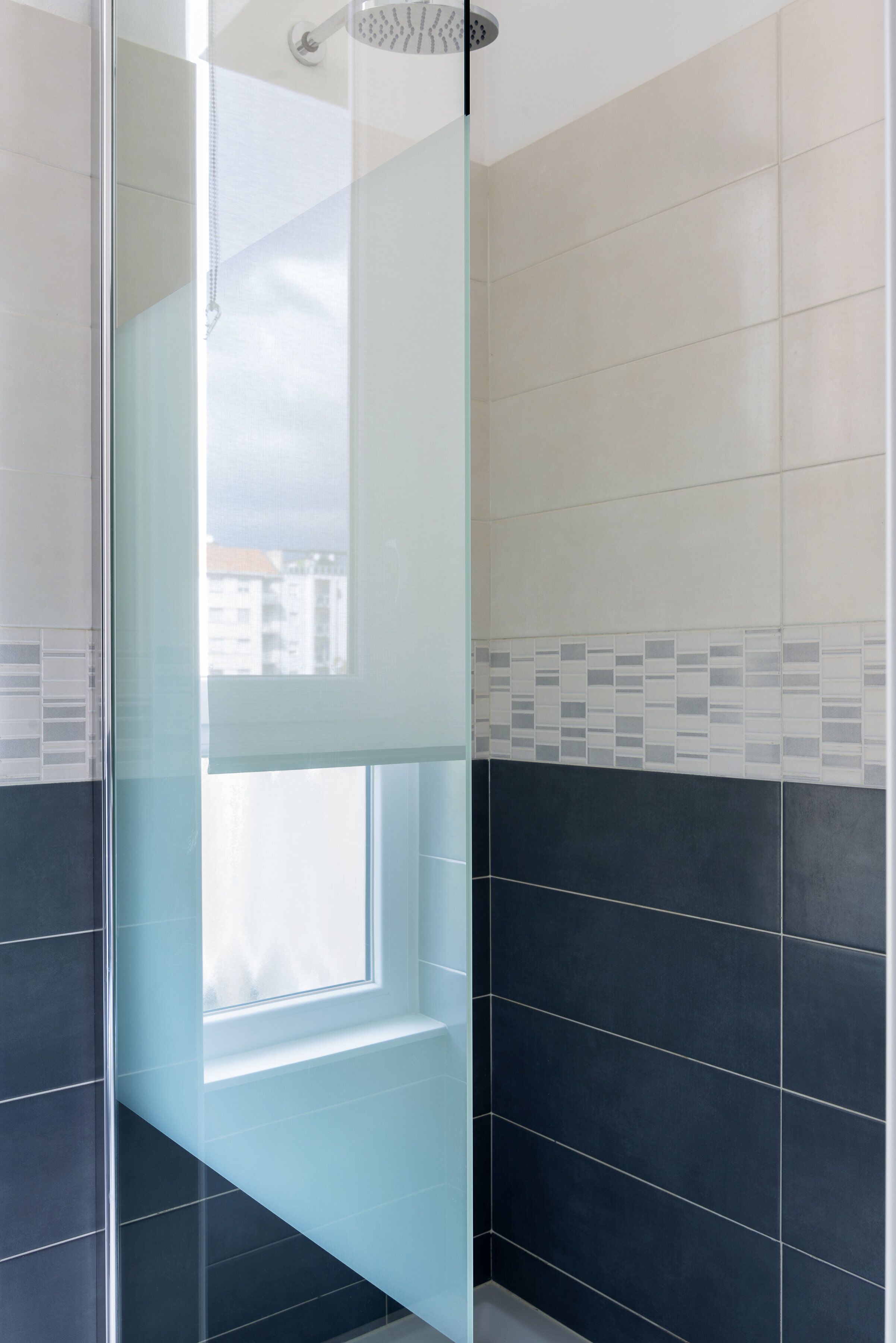 Une salle de bain moderne dotée d’une douche à parois de verre, d’une fenêtre et d’un mélange de carreaux clairs et foncés.