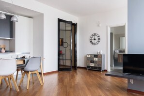A modern living room with a dining area, a TV, and a clock on the wall.