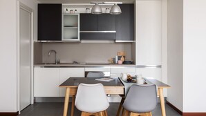 A modern kitchen with dark cabinets, a stainless steel sink, and a dining area with a wooden table and two chairs. - JOIVY Superb Flat W/Home Office (Milan)
