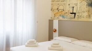 Et hotelværelse med en stor seng, hvide sengetøj og et vægmaleri.