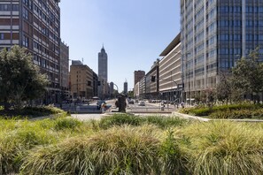 Une rue de la ville bordée d’immeubles modernes, une place centrale avec une statue, et un gratte-ciel imposant en arrière-plan.