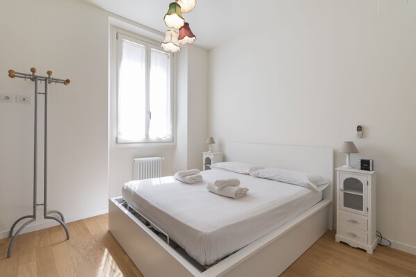 A minimalist bedroom with a bed, bedside lamps, a radiator, and a coat rack.