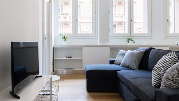 A modern living room with a flat-screen TV, a dark blue sofa, and a white console table. - JOIVY Lovely 1-Bed W/Balcony & Parking (Milan)