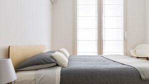 A bedroom with a bed, pillows, a bedside lamp, and a window with blinds. - JOIVY Lovely 1-Bed W/Balcony & Parking (Milan)