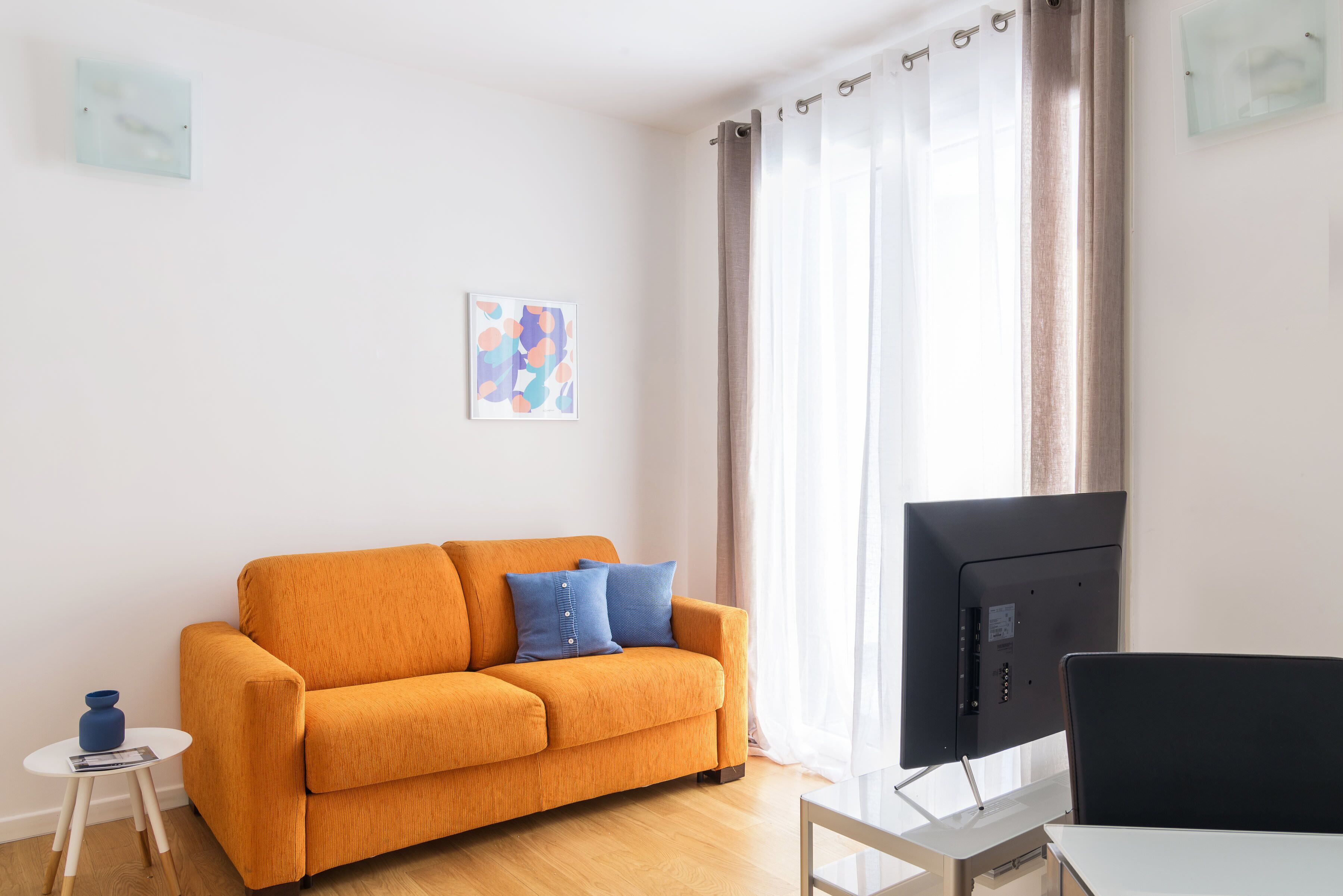 A modern living room with a sofa, a small table, a TV, and a window with curtains.
