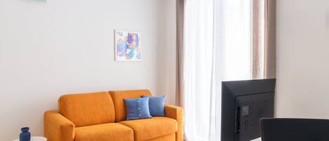 A modern living room with a sofa, a small table, a TV, and a window with curtains.