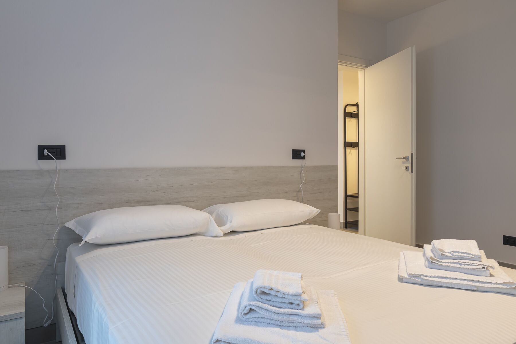 Une chambre d’hôtel comprenant un lit, deux tables de chevet, une commode, une prise électrique et une porte donnant accès à une salle de bain.