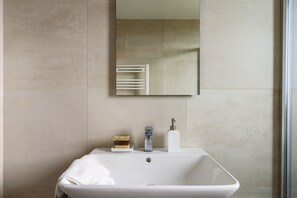 A bathroom with a white sink, a mirror, a towel, a soap dispenser, and a soap bar. - JOIVY Uptown Apartments (Milan)